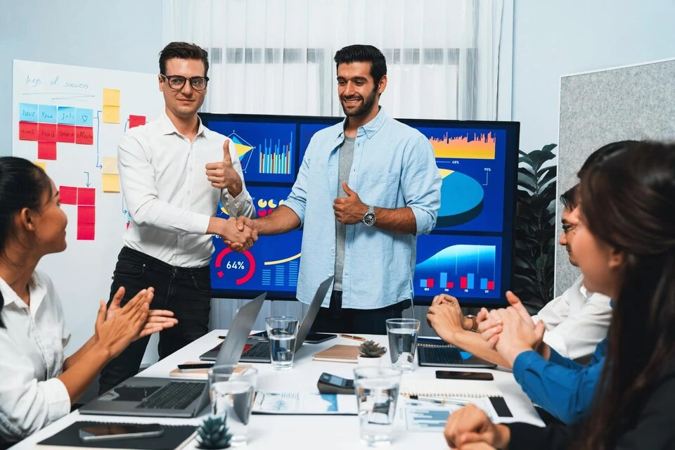 Business team celebrating after a successful data analysis meeting using the Best ERP Software in India, with analytics dashboards in the background